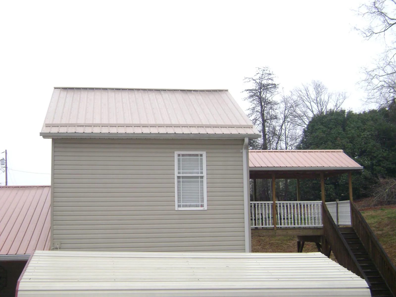 Tan metal roofs on a two story addition and attached porch, from a Roof Replacement job in Columbus